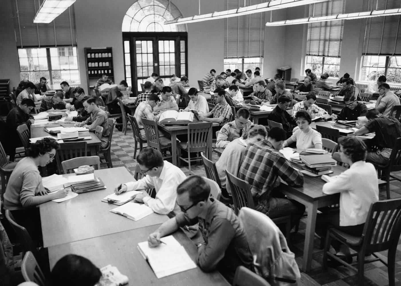 A black and white photo of students studying at long tables in a library